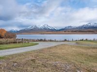 a park bench near a dirt road in an empty field near a lake and mountains