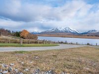 a park bench near a dirt road in an empty field near a lake and mountains