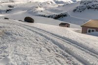 a snow covered slope with ski tracks and a building in the background and mountains,