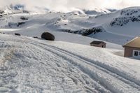 a snow covered slope with ski tracks and a building in the background and mountains,