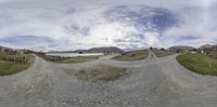 a long gravel road going down to a large body of water in the distance with some mountains in the background