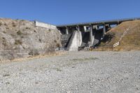 the concrete bridge crosses a gorge on a highway with a gate at one end, and a bench below