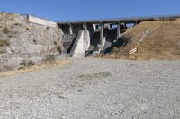 the concrete bridge crosses a gorge on a highway with a gate at one end, and a bench below