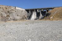 the concrete bridge crosses a gorge on a highway with a gate at one end, and a bench below