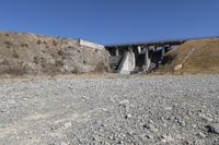 the concrete bridge crosses a gorge on a highway with a gate at one end, and a bench below