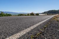 an empty road stretches on the edge of some hills and water is visible in the distance