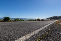 an empty road stretches on the edge of some hills and water is visible in the distance