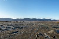 a tire tracks in an open land covered in snow and rock formations in the distance