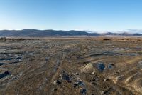 a tire tracks in an open land covered in snow and rock formations in the distance