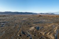 a tire tracks in an open land covered in snow and rock formations in the distance