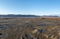 a tire tracks in an open land covered in snow and rock formations in the distance