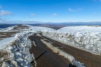 snow on the sides of the road with a mountain in the background under it and blue sky