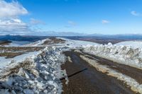 snow on the sides of the road with a mountain in the background under it and blue sky