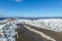 snow on the sides of the road with a mountain in the background under it and blue sky