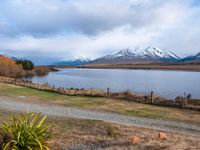 a road leading into the distance, with a lake in the foreground and snowy mountains