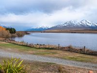 a road leading into the distance, with a lake in the foreground and snowy mountains