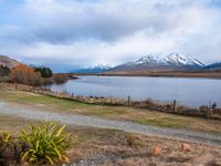 a road leading into the distance, with a lake in the foreground and snowy mountains