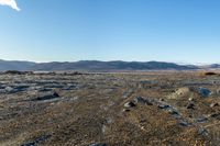 a field with a few rocks and a body of water in the distance, a mountains and blue sky