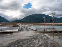 a train crossing bridge with a truck approaching the train station in the background of mountains