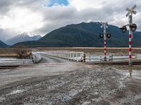 a train crossing bridge with a truck approaching the train station in the background of mountains