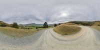 dirt road with a mountain in the distance under clouds and rain clouds passing overhead and on to grass covered hill