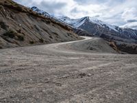 a dirt road going up a mountain side with snow covered mountains in the distance on both sides