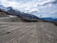 a dirt road going up a mountain side with snow covered mountains in the distance on both sides