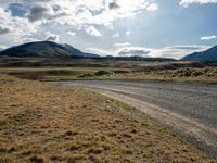 a dirt road running through mountains near grass and grass covered fields with a yellow sign in front