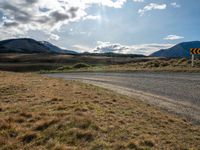 a dirt road running through mountains near grass and grass covered fields with a yellow sign in front