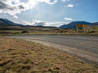 a dirt road running through mountains near grass and grass covered fields with a yellow sign in front