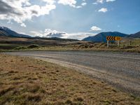 a dirt road running through mountains near grass and grass covered fields with a yellow sign in front