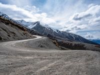 a dirt road running down a mountain side near a mountainous landscape with snow capped mountains