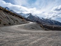 a dirt road running down a mountain side near a mountainous landscape with snow capped mountains