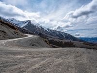 a dirt road running down a mountain side near a mountainous landscape with snow capped mountains