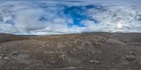 the image shows a mountain under a cloudy sky and clouds above it with rocks on a dirt hill in front of the mountain