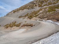 the winding road on the hill is made up by a stone wall and snow in a mountainous area