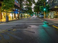 a lone street at night, the green traffic lights are lit up at the intersection