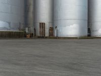 a skateboarder is doing tricks on a cement surface near a silos in an urban setting