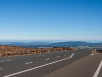 a road with a sky background with mountains in the distance and an airplane flying over