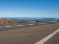 a road with a sky background with mountains in the distance and an airplane flying over