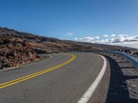 an empty road with curves between two lanes with a person on a motorcycle in the distance