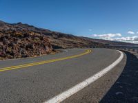 an empty road with curves between two lanes with a person on a motorcycle in the distance