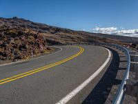 an empty road with curves between two lanes with a person on a motorcycle in the distance