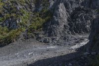 a small mountain is shown with a man walking by it and the top half has mossy rocks