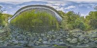 a circular, green tunnel with rocks and trees near by on the bank of the river