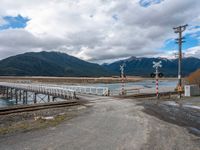 a railroad crossing with a body of water and some mountains in the background of this image