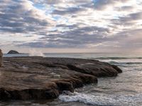 a man standing on top of a stone cliff next to the ocean next to rocks