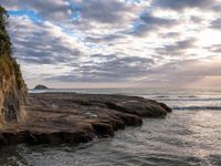 a man standing on top of a stone cliff next to the ocean next to rocks