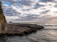 a man standing on top of a stone cliff next to the ocean next to rocks