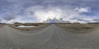 a 360 - vision photo of a road with cloudy skies and mountain peaks in the background